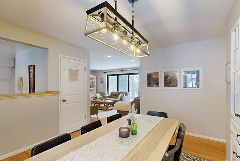 Modern dining area featuring a long table, pendant lighting, and views into a cozy living space with artwork on the walls.