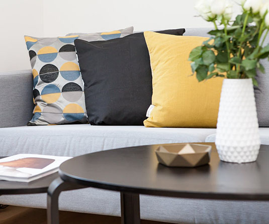 A stylish living room scene featuring a gray sofa with patterned pillows, a round black coffee table, and a vase of white roses.